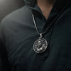 Man wearing a detailed silver round pendant necklace with engraved bearded figure