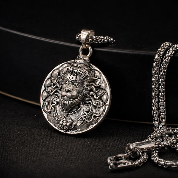 Antique silver tone pendant necklace with intricate deity face design on dark background