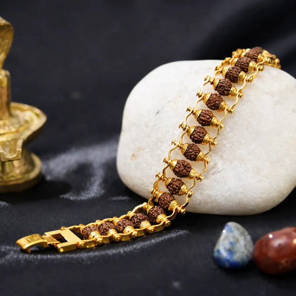 Rudraksha and gold chain bracelet displayed on white stone with decorative elements