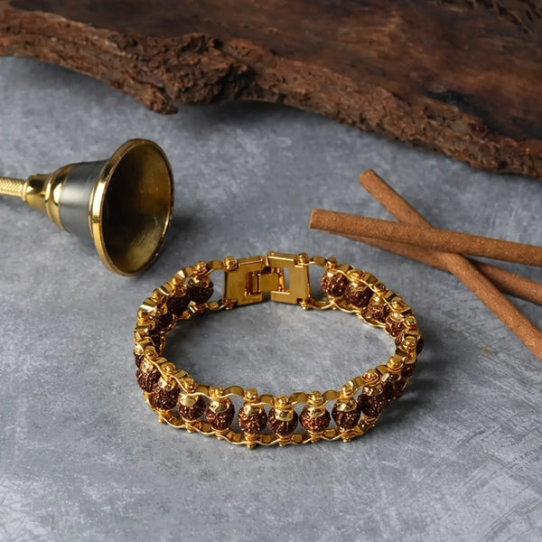 Rudraksha and gold tone bracelet on stone surface with cinnamon sticks and a brass bell