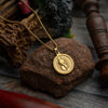 Gold pendant necklace with engraved warrior design displayed on a stone background