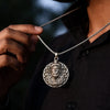 Hand holding silver medallion necklace with intricate lion face pendant, worn on black shirt
