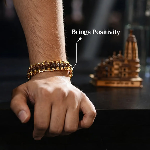 Hand wearing a gold chain Rudraksha bracelet, brings positivity, with temple model on table