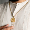 Gold round pendant necklace with intricate Hindu deity design worn on beige kurta