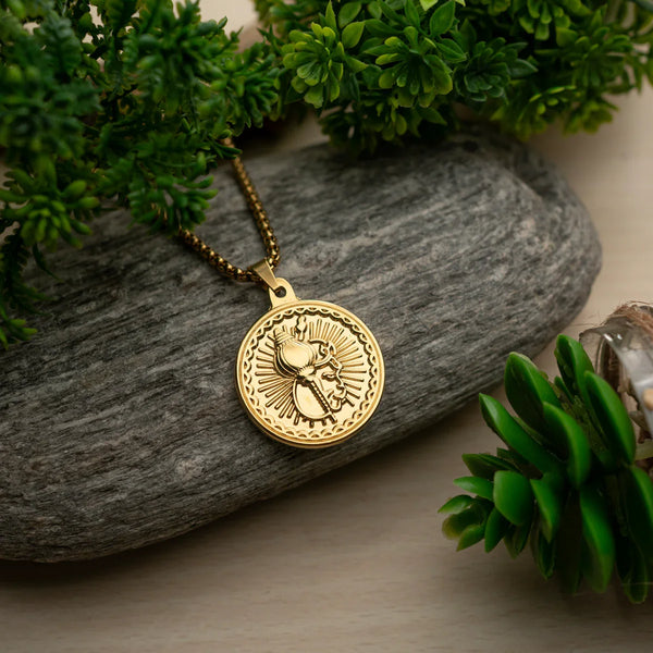 Gold round pendant with engraved beetle design on chain, displayed on stone with green plants