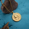 Gold round pendant necklace with sacred symbols on blue textured surface