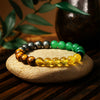 Multicolored gemstone beaded bracelet on stone, with green, yellow, brown, and gray beads